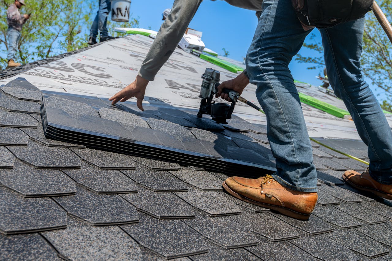 Roofer using nail gun for shingle installation on residential roof.